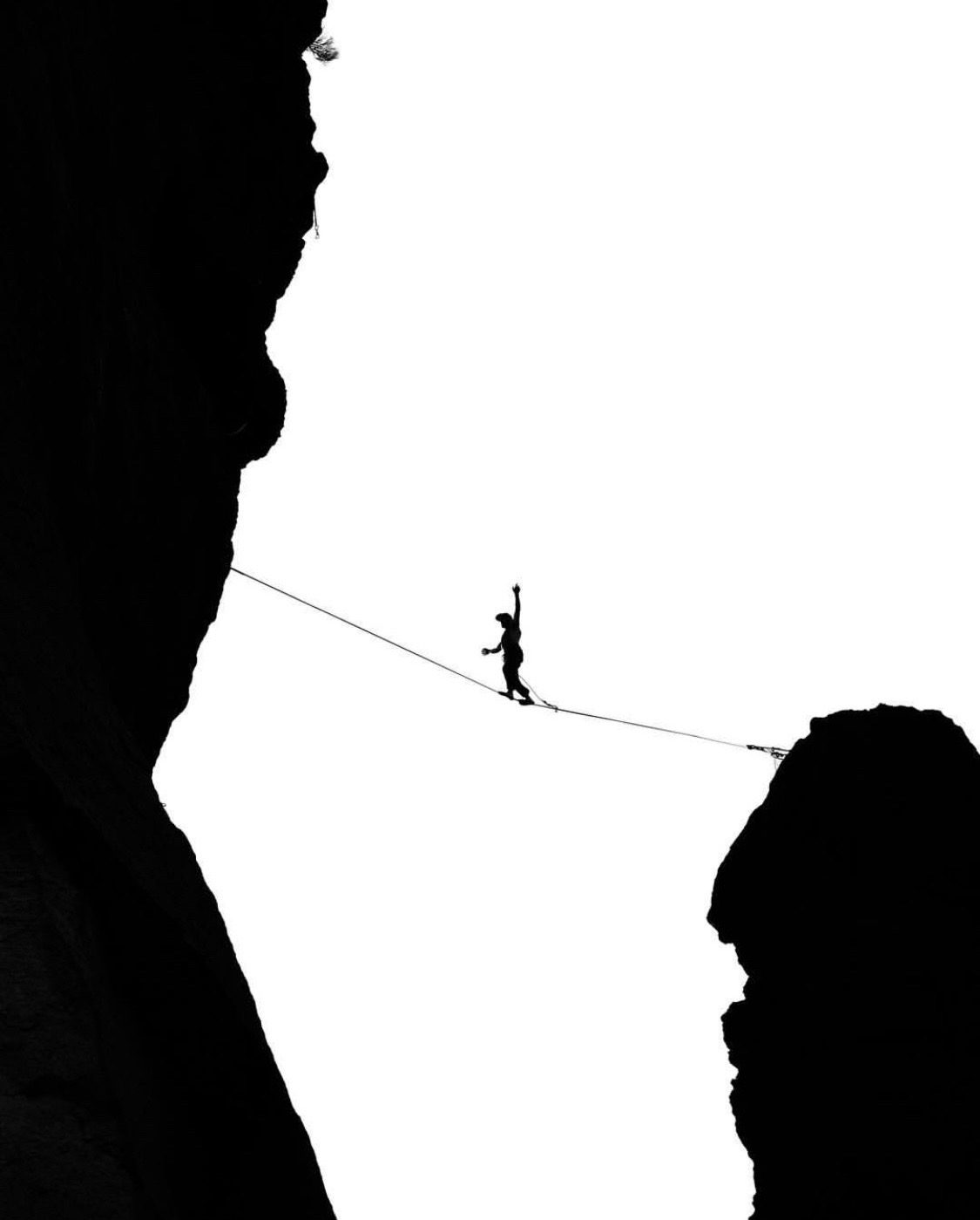 Black and white silhouette highlining between cliffs